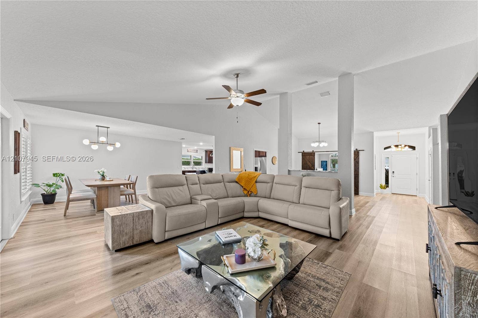 Vaulted ceilings, wood-finish flooring, ceiling fan with integrated lighting, and multi-light pendant chandeliers