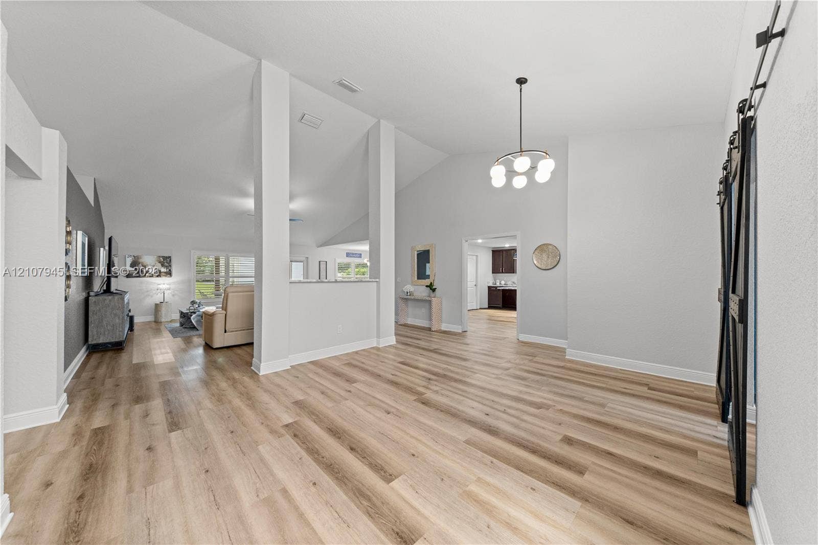 Vaulted ceilings, wood-finish flooring, architectural support pillars, and black metal sliding barn door hardware