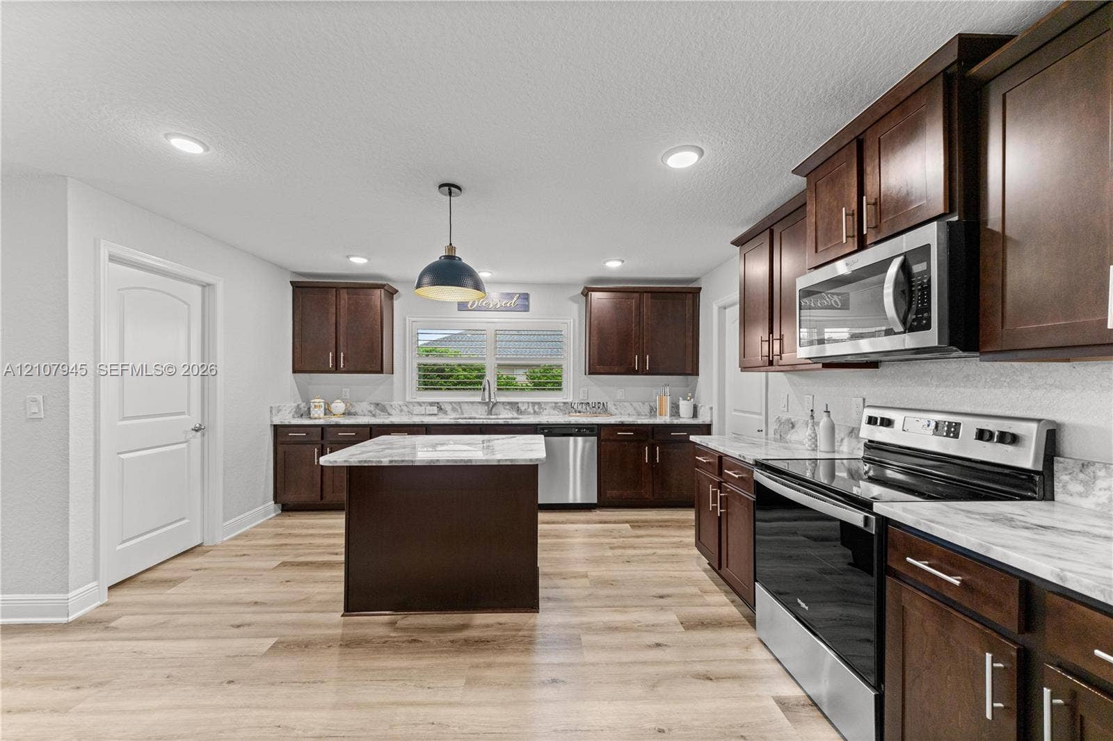 Kitchen featuring dark-finish cabinetry, stone-patterned countertops, a center island, stainless steel appliances, and wood-finish flooring