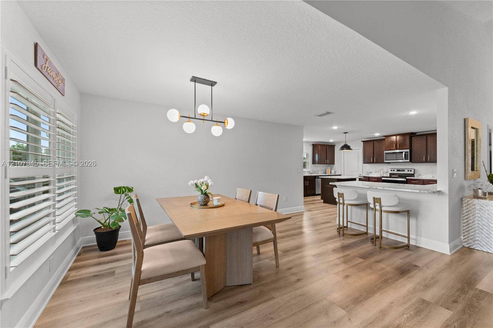 Dining area featuring wood-finish flooring, a contemporary six-light globe chandelier, and white plantation shutters