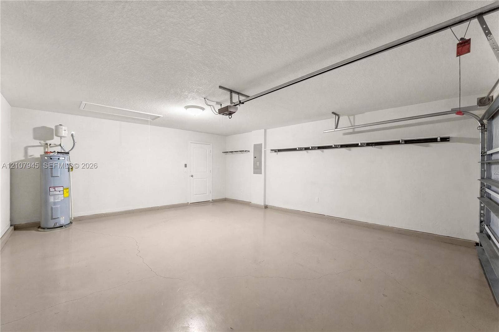 Attached garage featuring painted concrete flooring, wall-mounted storage rack, overhead lighting, and dedicated water heater housing