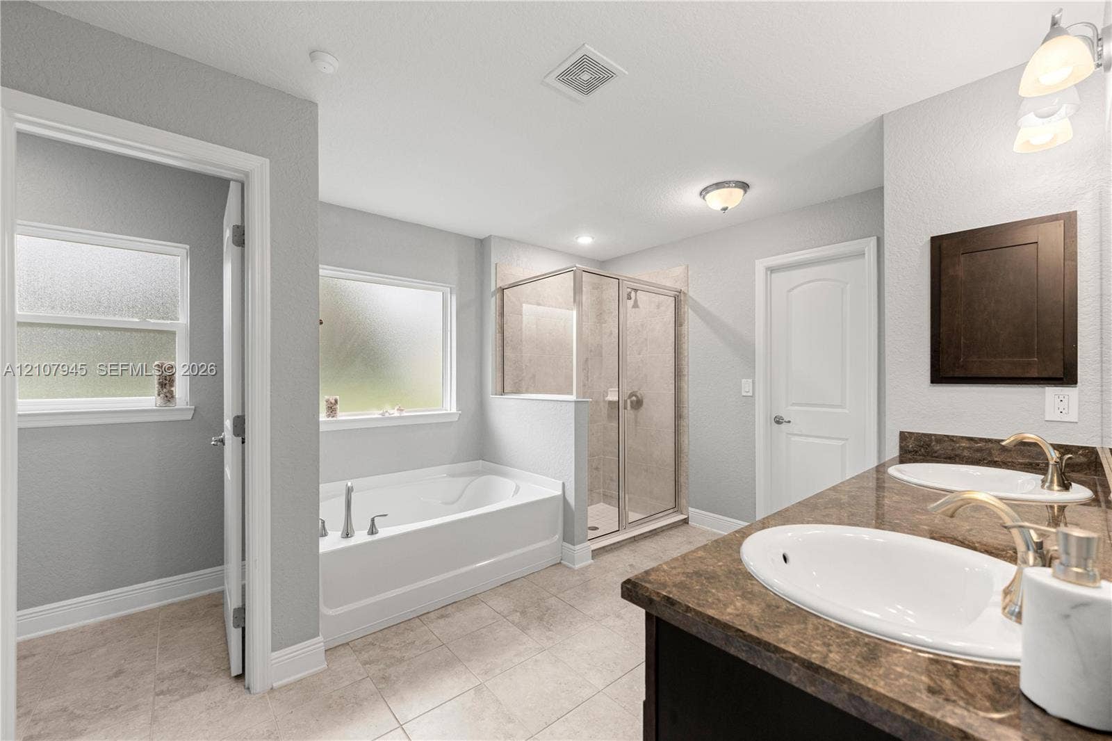 Bathroom featuring a dual-sink vanity with a dark-finish cabinet and solid-surface countertop, a separate deep soaking tub, and a glass-enclosed shower