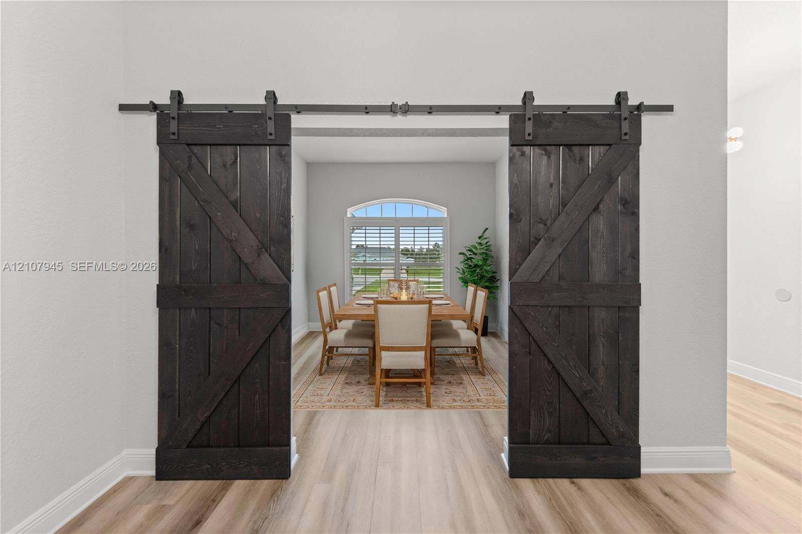 Dark-stained wood barn doors featuring a cross-brace design with matte black hardware, paired with light-toned wood-finish flooring and an arched window
