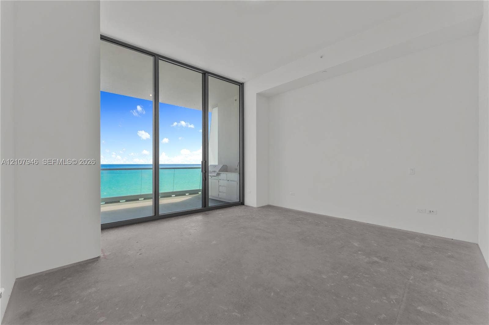 Floor-to-ceiling glass panel doors, polished concrete flooring, white walls, and a balcony featuring a built-in outdoor kitchen with stone surfacing