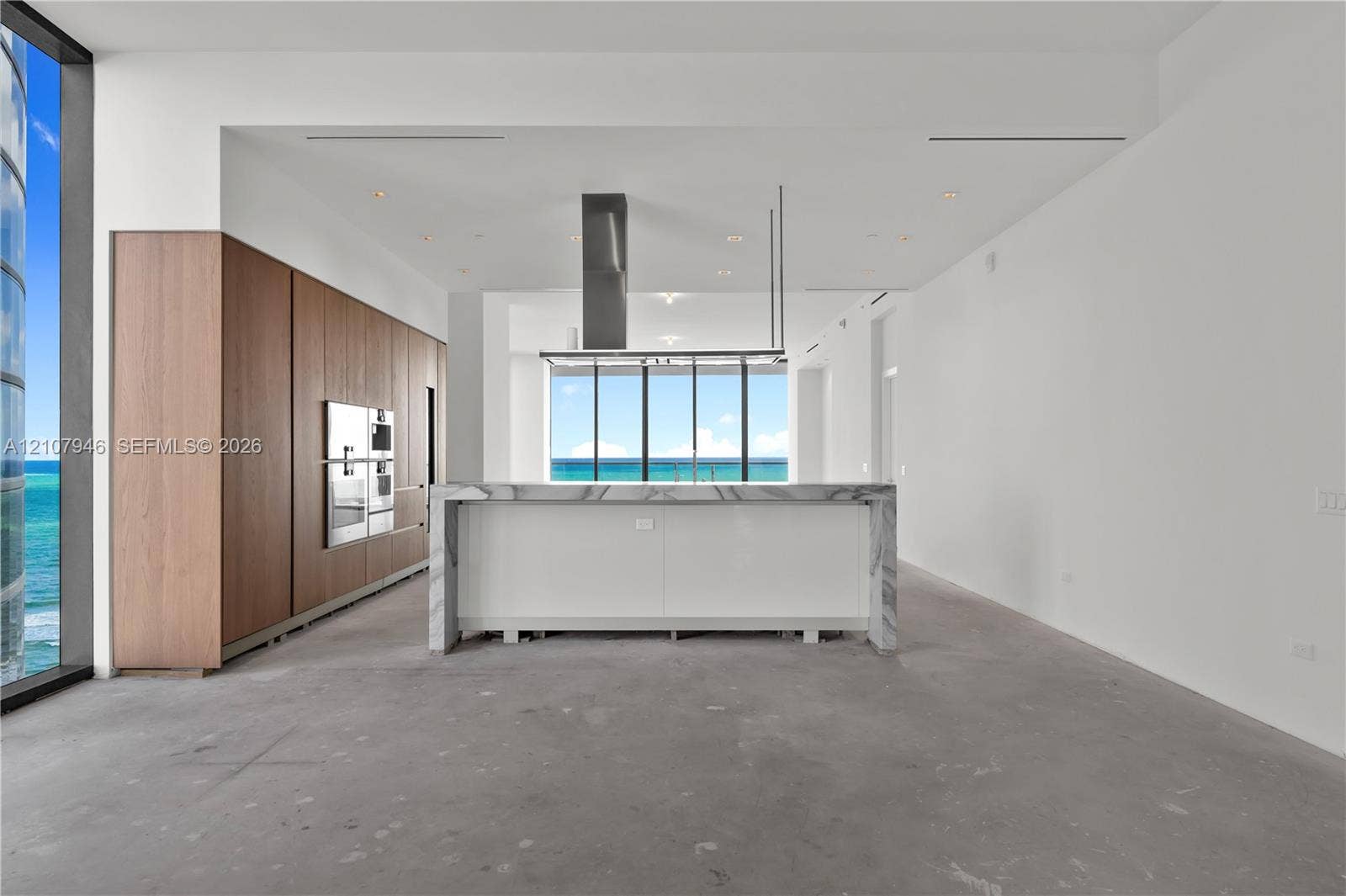 Contemporary kitchen featuring full-height wood cabinetry, a waterfall-edge stone island, built-in stainless steel appliances, a ceiling-mounted range hood, and floor-to-ceiling windows
