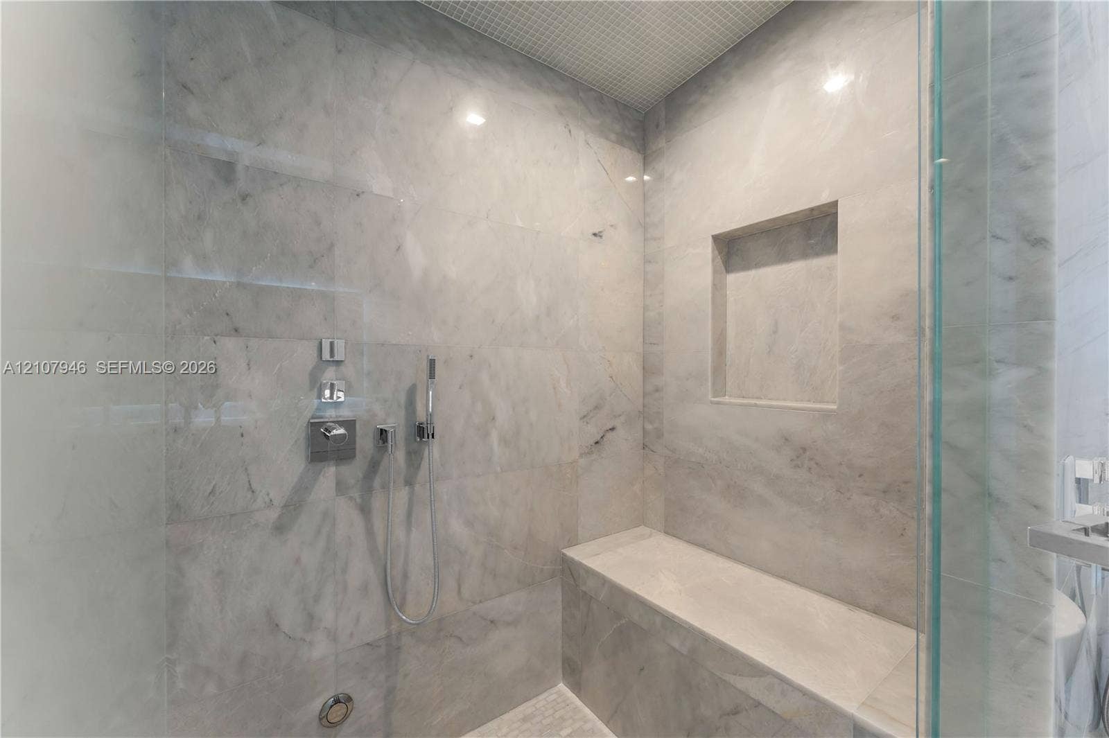 Walk-in shower featuring floor-to-ceiling stone tile, a built-in bench, integrated wall niche, and polished chrome hardware