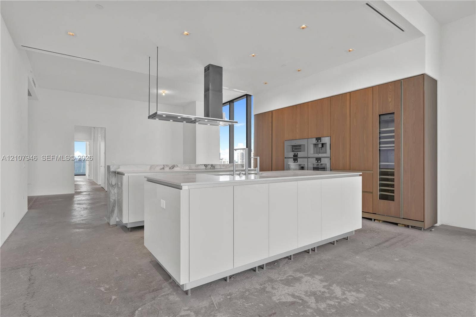 Kitchen featuring a large central island with solid-surface countertop, floor-to-ceiling wood-finish cabinetry, integrated built-in appliances, a stainless steel range hood, and recessed lighting