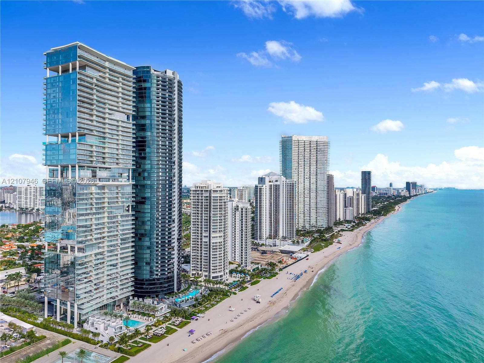 High-rise residential tower featuring glass-paneled exterior, deep recessed balconies, direct oceanfront positioning, and ground-level pool amenities