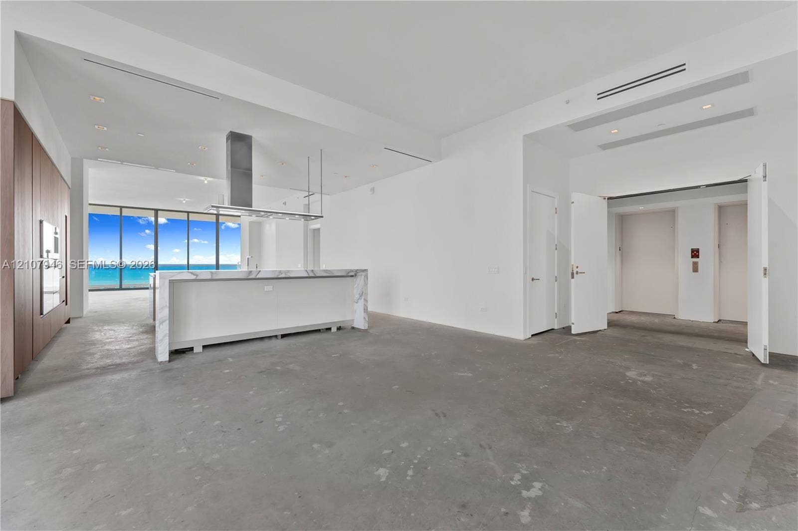 Open concept interior featuring a kitchen island with stone-finish waterfall edges, floor-to-ceiling windows, stainless steel vent hood, and full-height wood-finish cabinetry