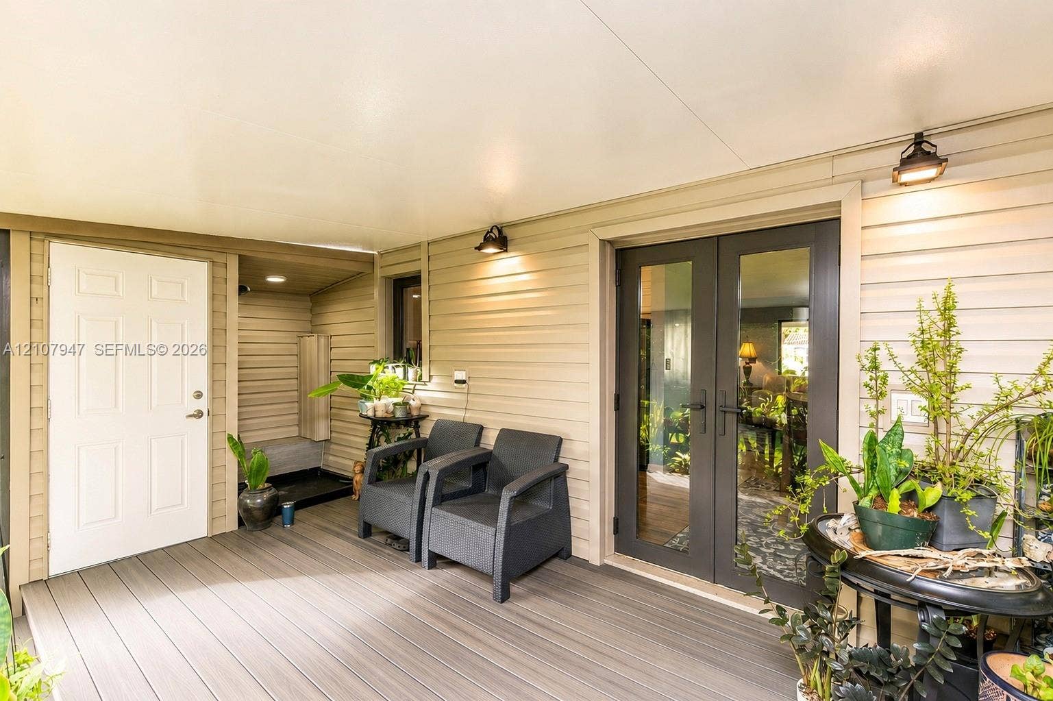 Covered porch featuring composite decking, horizontal siding, double-glass entry doors, and wall-mounted exterior lighting
