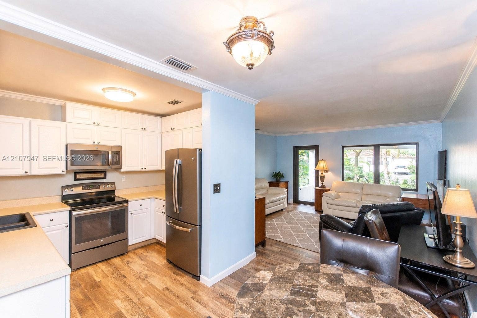 Kitchen featuring white cabinetry, stainless steel appliances, and wood-finish flooring, complemented by a semi-open floor plan with crown molding