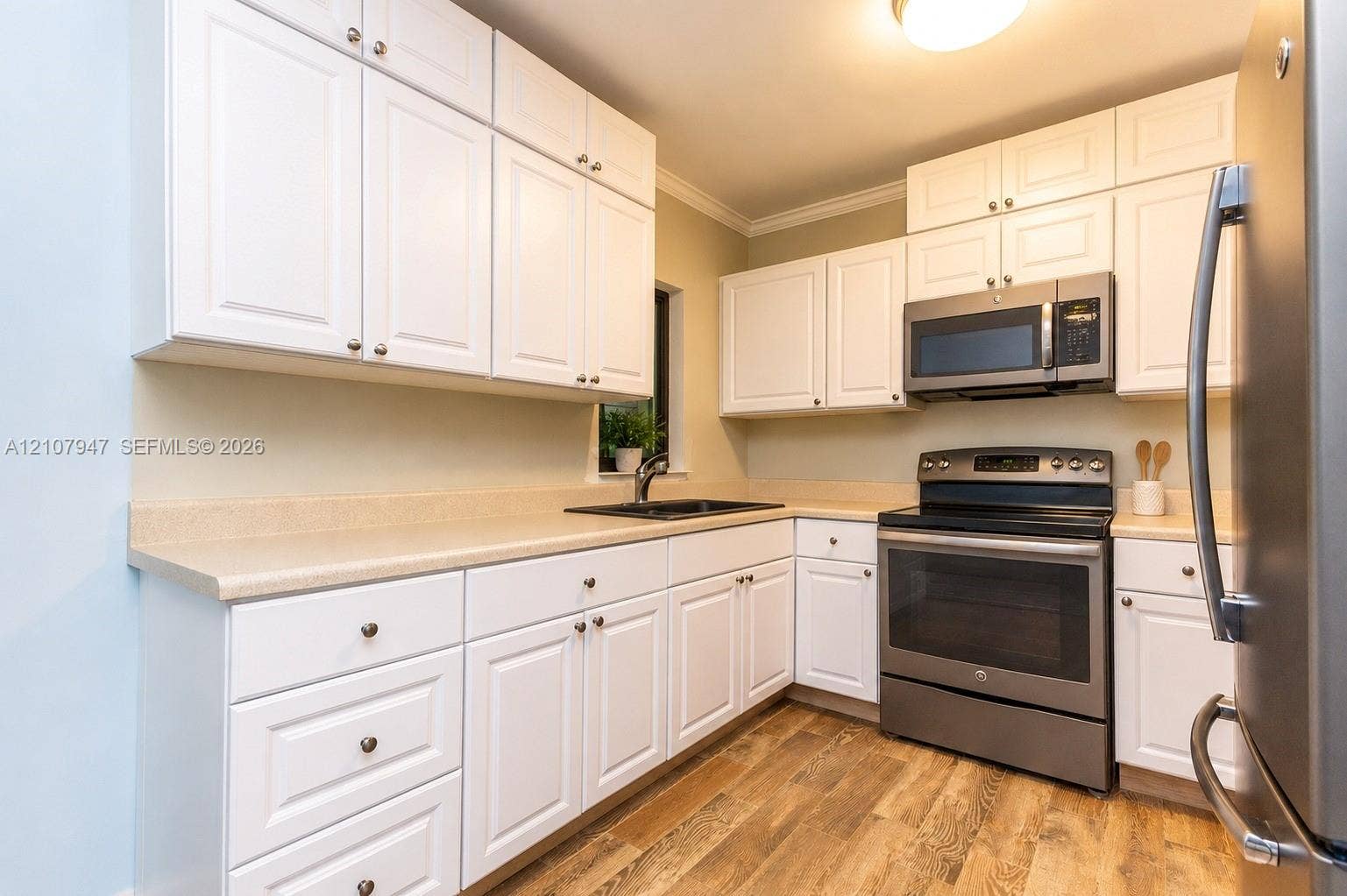 Kitchen featuring white shaker-style cabinetry, solid-surface countertops, wood-finish flooring, and stainless steel appliances