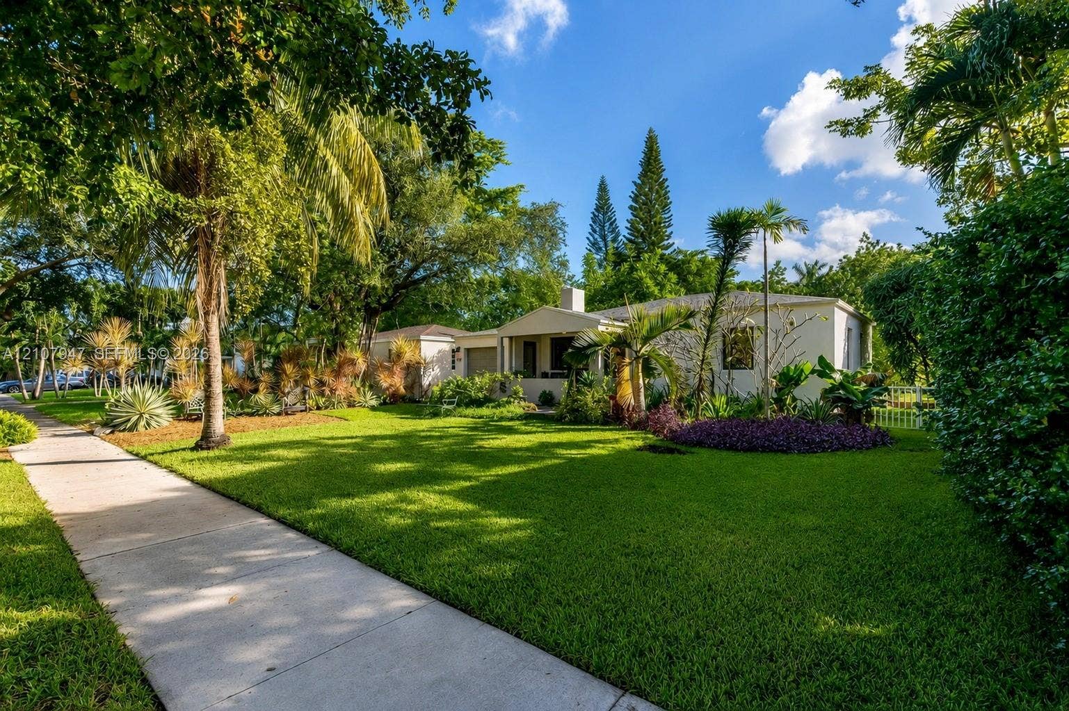 Single-story residence featuring a concrete exterior, covered entryway, manicured lawn, and mature landscaping