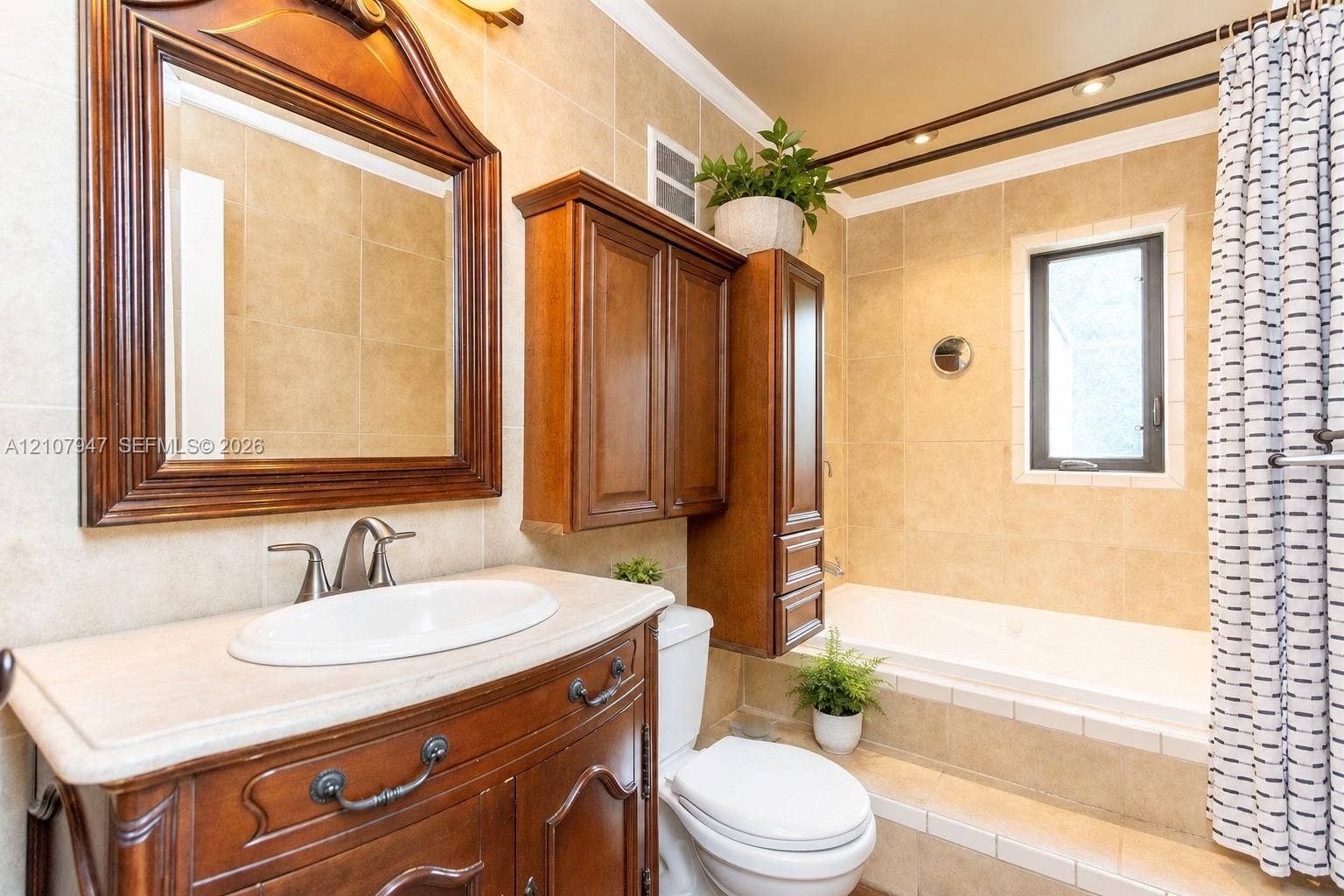 Bathroom featuring a wood vanity with an integrated oval sink and stone-finish countertop, matching wood-frame wall mirror, wall-mounted wood cabinetry, built-in soaking tub with a tile surround, and neutral wall tile throughout