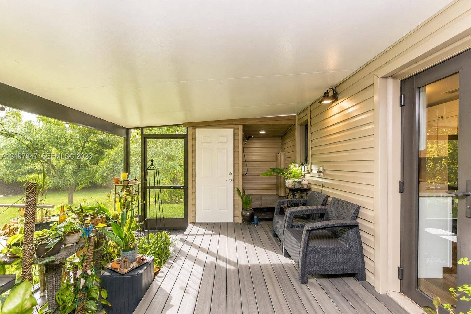 Covered screened-in patio featuring composite decking, vinyl siding, a dedicated exterior door, and wall-mounted lighting