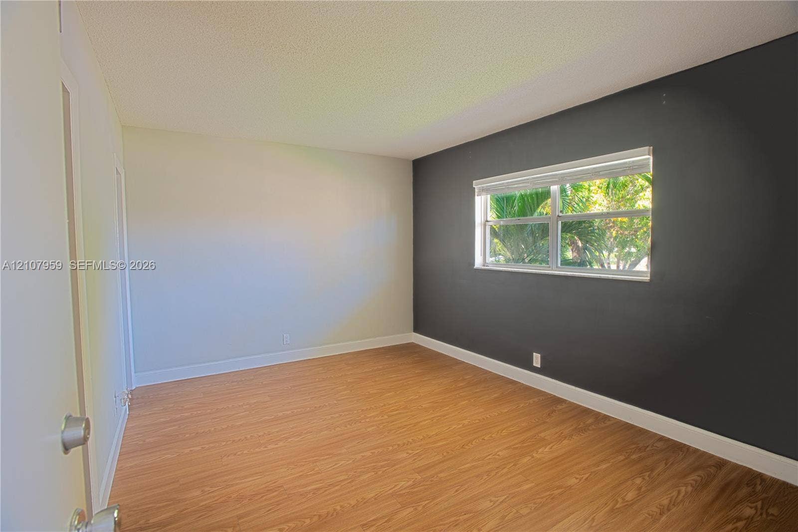 4200 Crystal Lake Drive, #204, Deerfield Beach, Deerfield Beach, FL 33064 Room featuring wood-finish flooring, a dark charcoal accent wall, neutral painted walls, and a horizontal window with a fitted roller shade