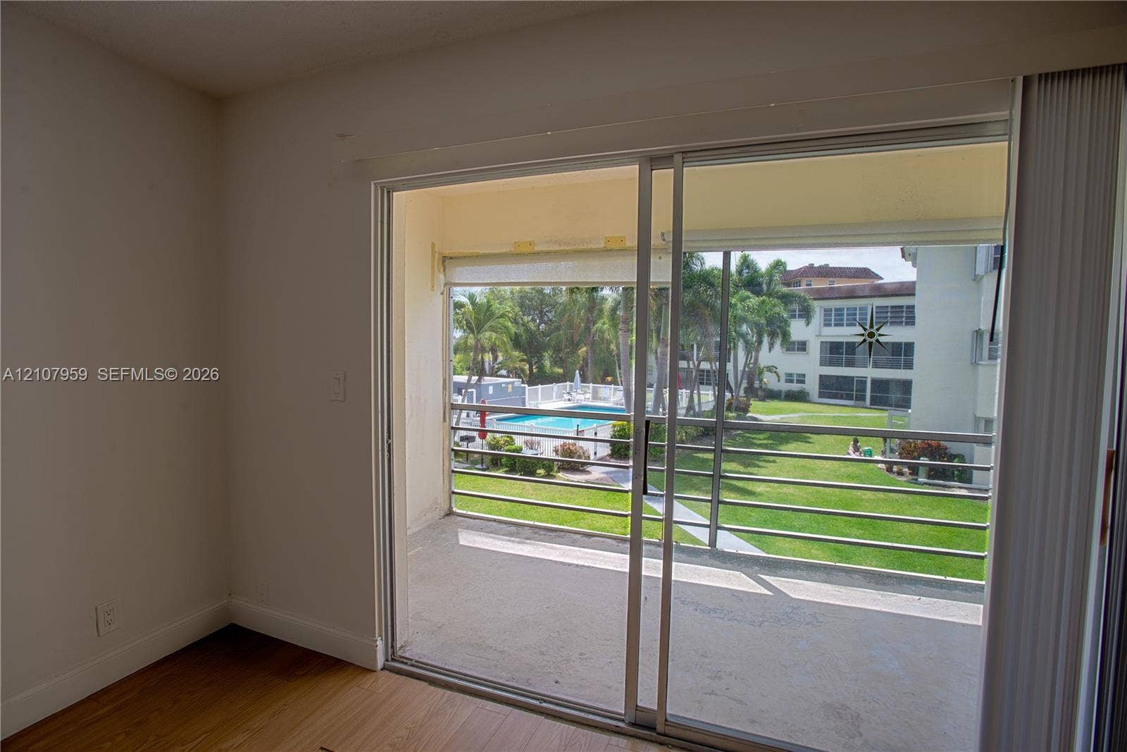 4200 Crystal Lake Drive, #204, Deerfield Beach, Deerfield Beach, FL 33064 Sliding glass door opening to a private balcony featuring metal railings, wood-finish flooring, and exterior exposure to a swimming pool and landscaped grounds