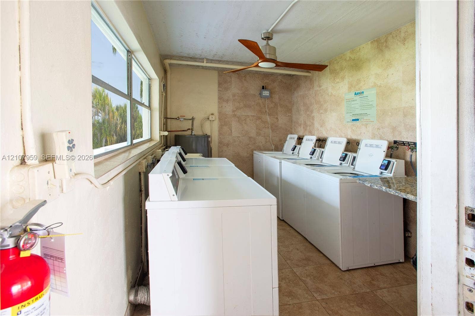 4200 Crystal Lake Drive, #204, Deerfield Beach, Deerfield Beach, FL 33064 Utility space featuring stone tile wall cladding and flooring, a ceiling fan, and multiple top-load washer and dryer units with stone countertop surfacing