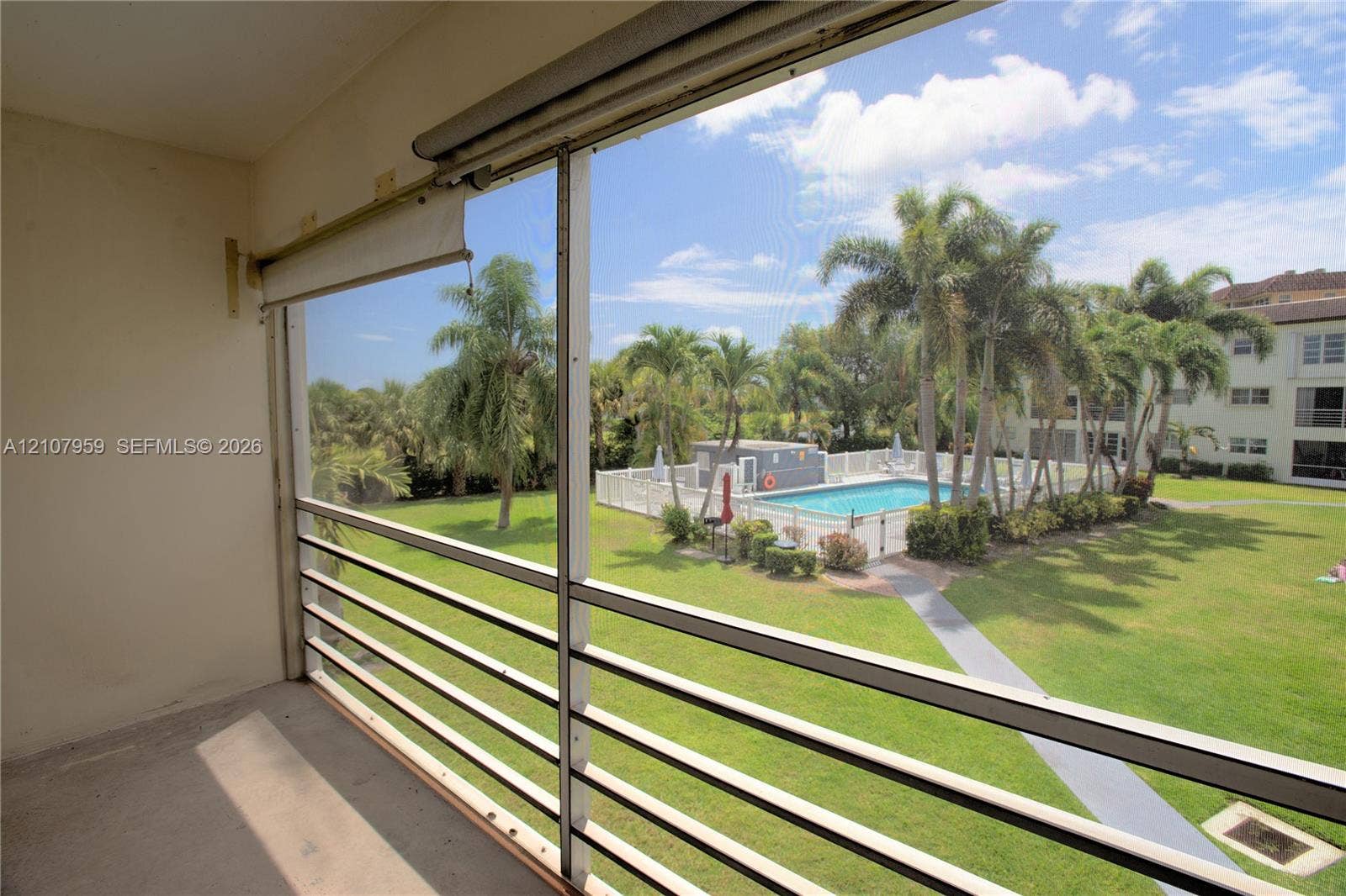 4200 Crystal Lake Drive, #204, Deerfield Beach, Deerfield Beach, FL 33064 Screened-in balcony featuring metal railing, outdoor pool, paved walkway, and landscaped grounds