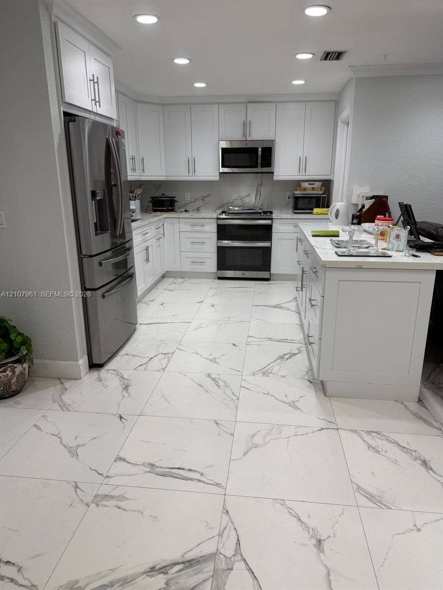 Kitchen featuring white shaker-style cabinetry, stainless steel appliances, a central island with a stone-finish countertop, and large-format tile flooring with a veined pattern
