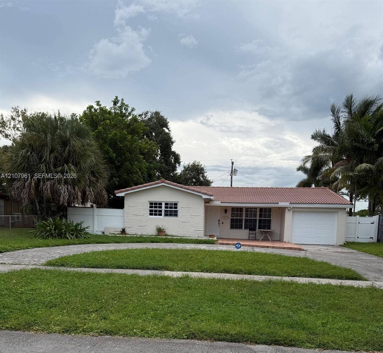 Single-story residence featuring a tile roof, stucco exterior, attached garage, and white vinyl privacy fencing