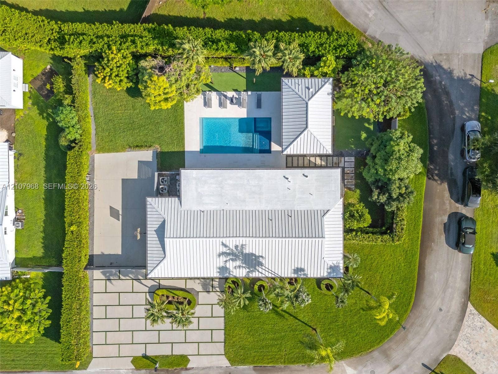 10841 SW 126th Street, Miami, FL 33176 Aerial view of property featuring a metal roof, rectangular swimming pool, expansive concrete paver driveway, manicured lawn, and mature perimeter hedging