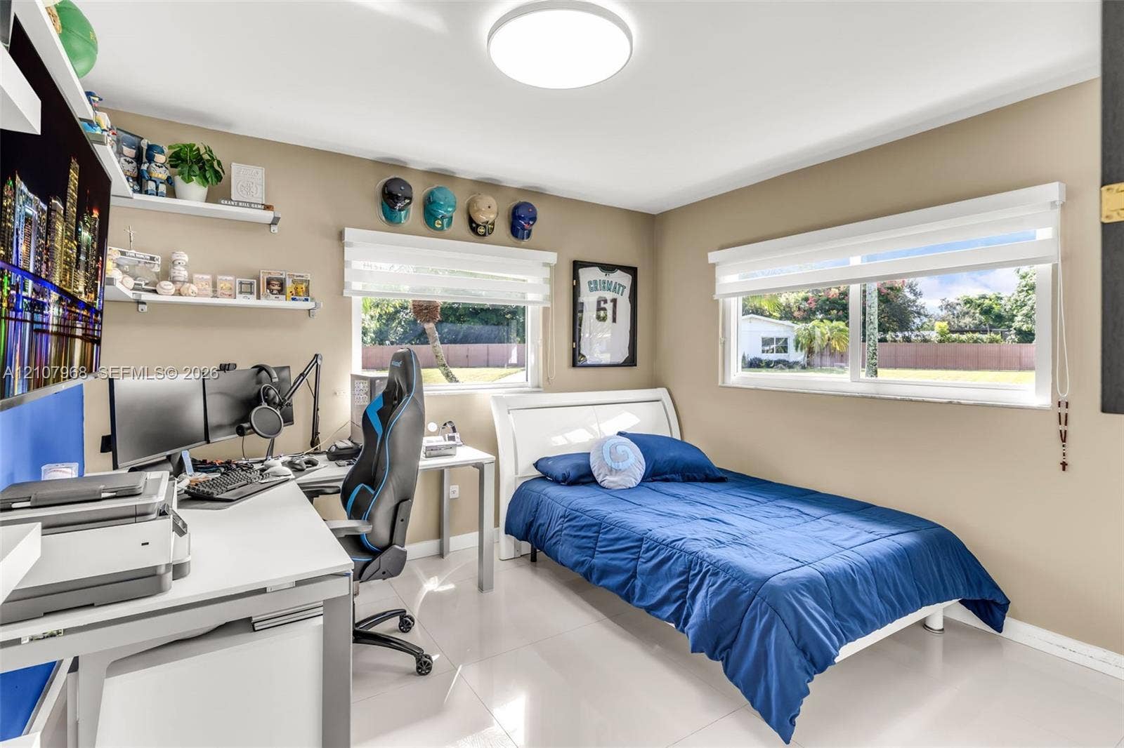 10841 SW 126th Street, Miami, FL 33176 Bedroom featuring glossy tile flooring, neutral wall tones, dual horizontal windows with roller shades, built-in white shelving, and a flush-mount circular ceiling light fixture