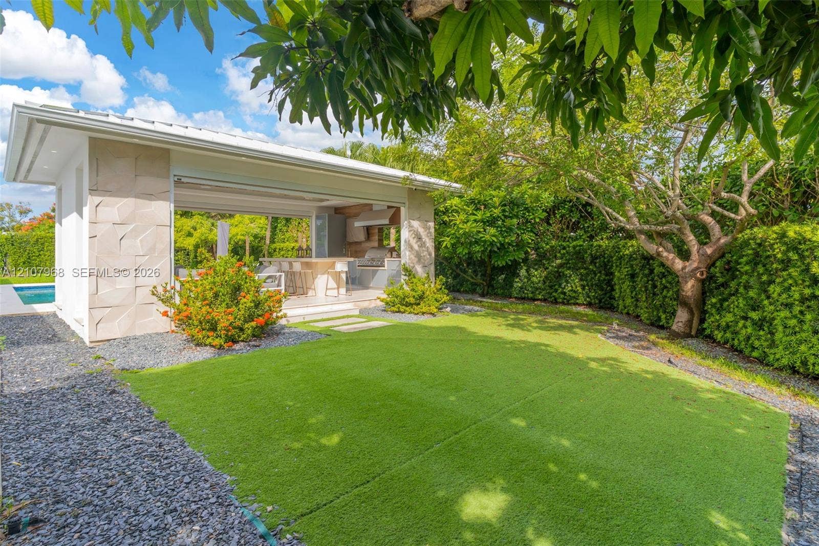 10841 SW 126th Street, Miami, FL 33176 Outdoor pavilion featuring a textured stone facade, integrated built-in kitchen, low-maintenance turf lawn, and perimeter landscaping