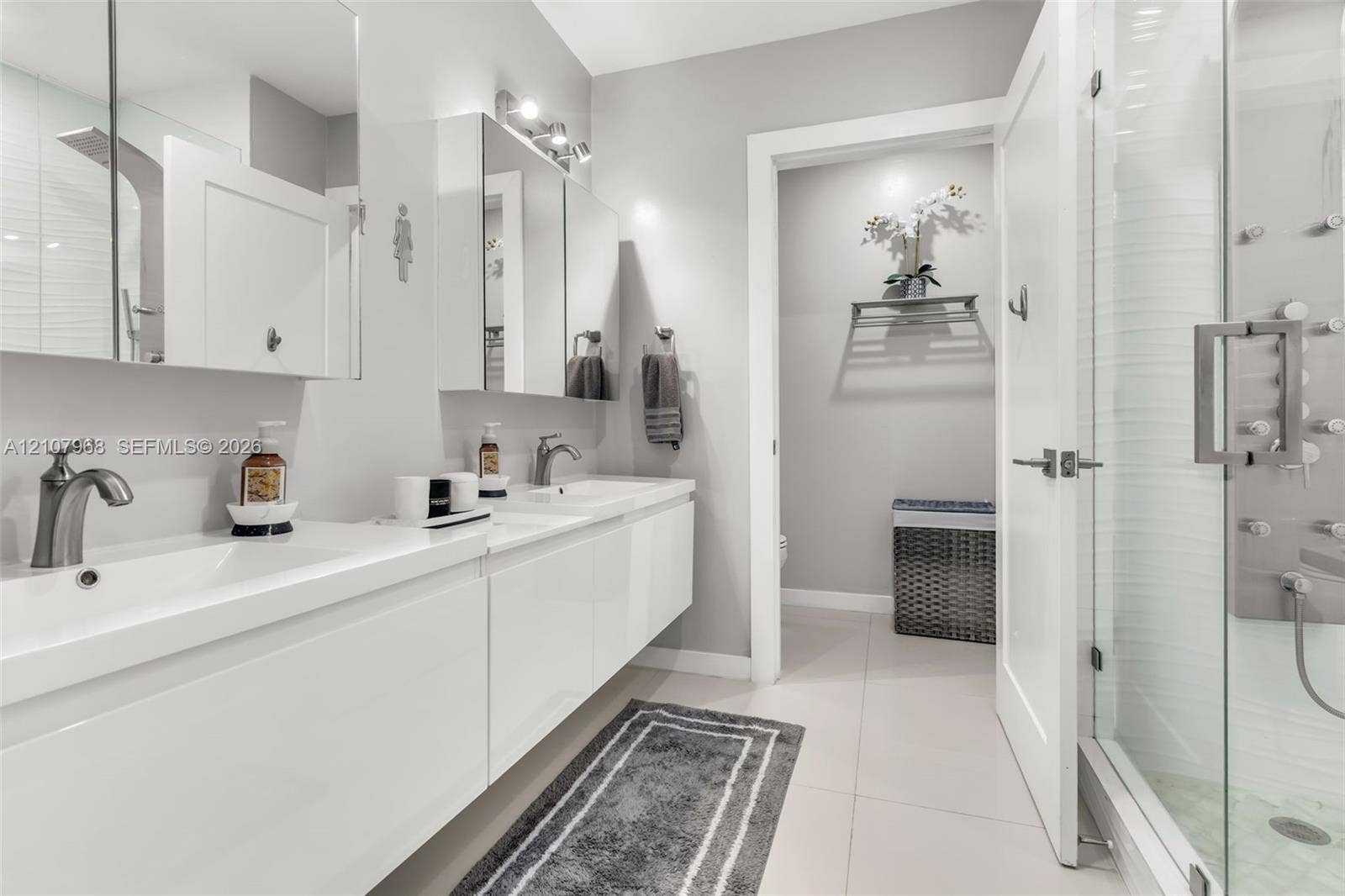 10841 SW 126th Street, Miami, FL 33176 Dual-sink floating vanity with white cabinetry, integrated rectangular basins, and brushed-nickel faucets, complemented by a walk-in glass shower featuring multiple body spray jets and a tiled floor