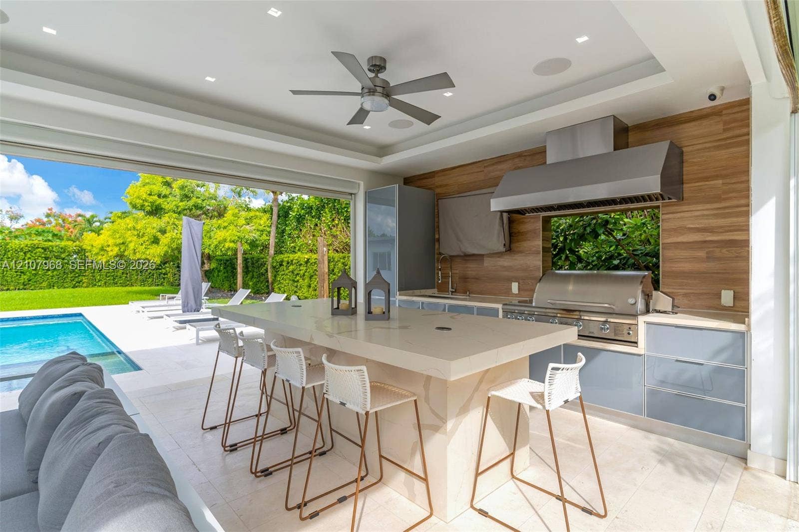 10841 SW 126th Street, Miami, FL 33176 Covered outdoor kitchen featuring a stone-topped island, stainless steel grill, professional-grade range hood, wood-finish wall paneling, and recessed lighting