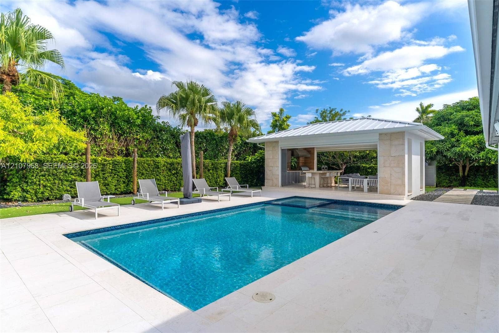 10841 SW 126th Street, Miami, FL 33176 In-ground swimming pool with a stone patio, accompanied by a covered pavilion featuring a built-in outdoor kitchen and stone support columns
