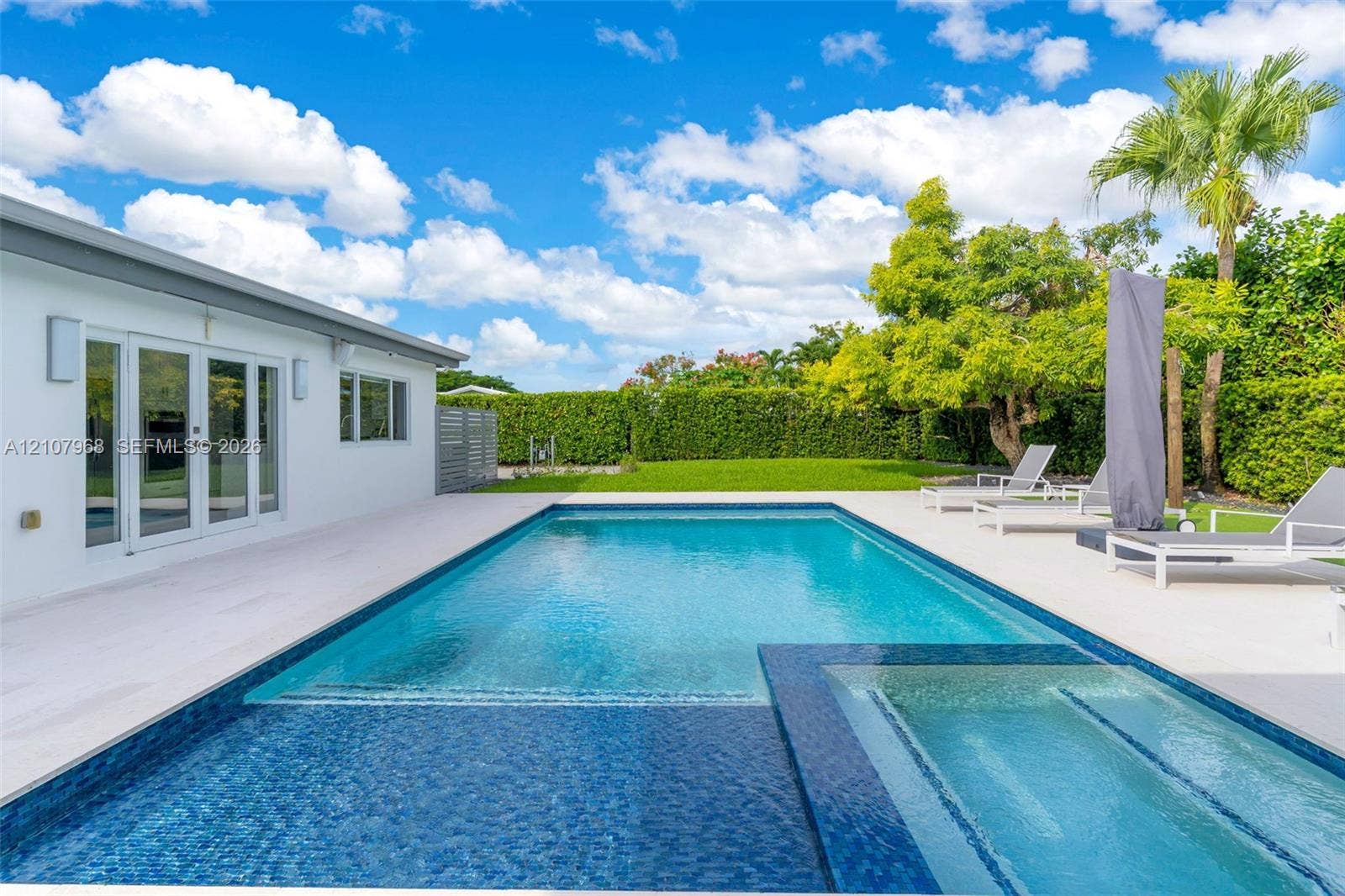 10841 SW 126th Street, Miami, FL 33176 Backyard featuring a custom swimming pool with integrated spa, tile finish, expansive light-toned hardscaping, and privacy hedge