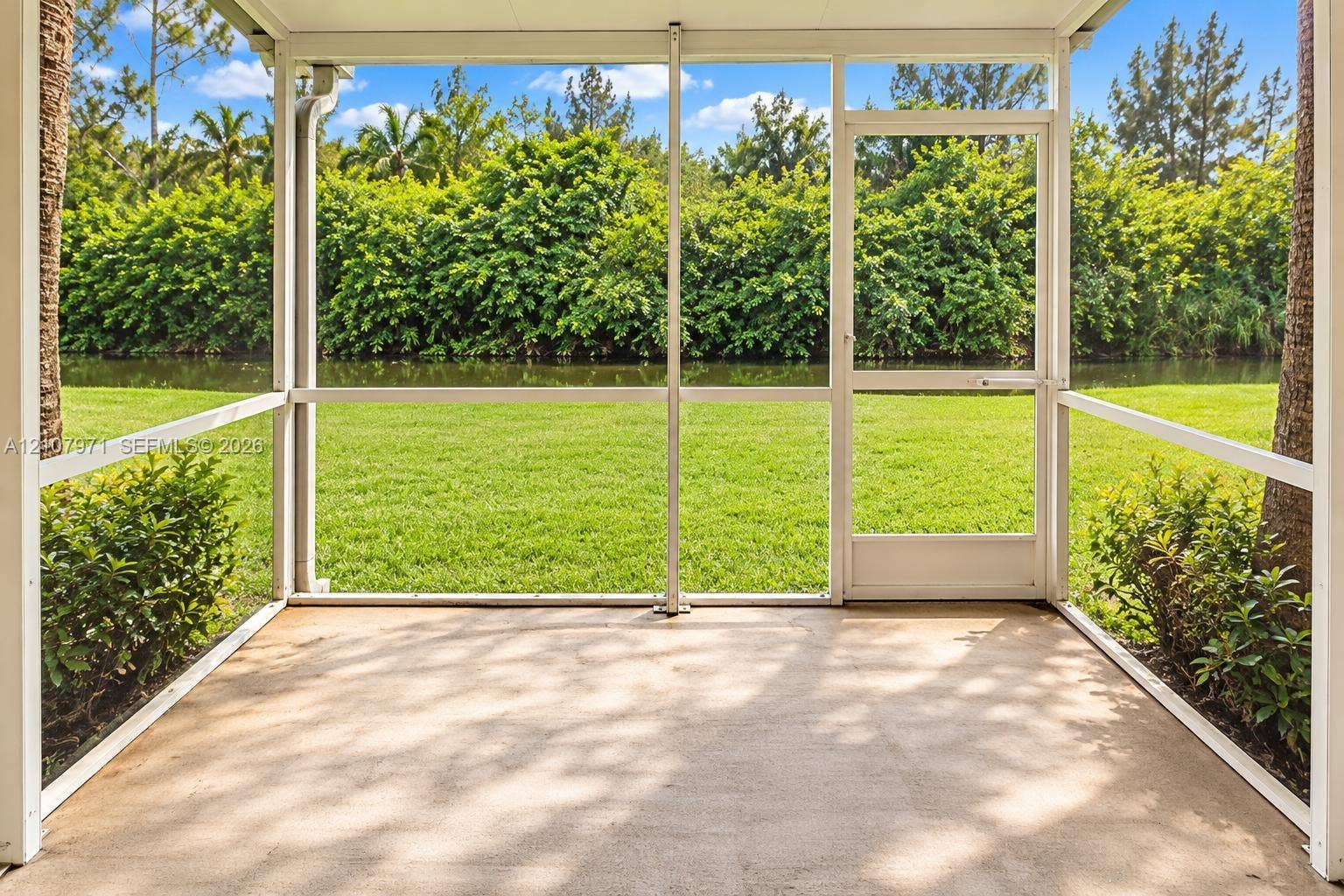4921 SW 66th Terrace, #4921, Davie, Davie, FL 33314 Screened-in patio with concrete flooring, aluminum framing, and a full-height entry door, overlooking a lawn and waterfront