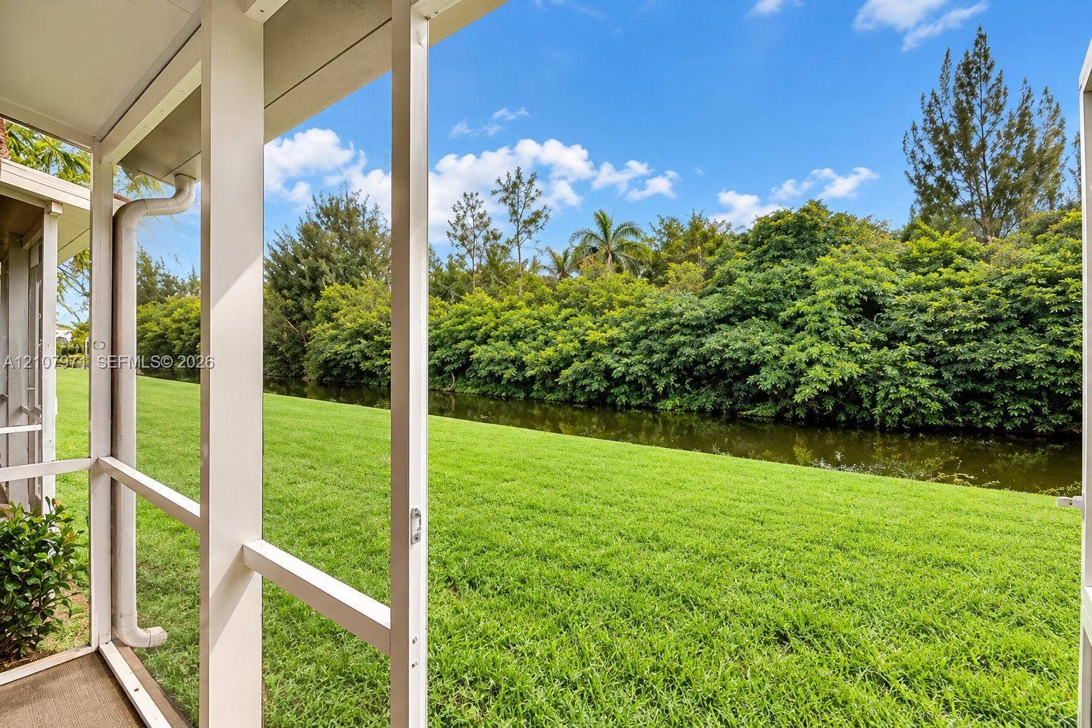4921 SW 66th Terrace, #4921, Davie, Davie, FL 33314 Screened-in porch featuring white structural framing, expansive lawn, mature tree line, and water frontage
