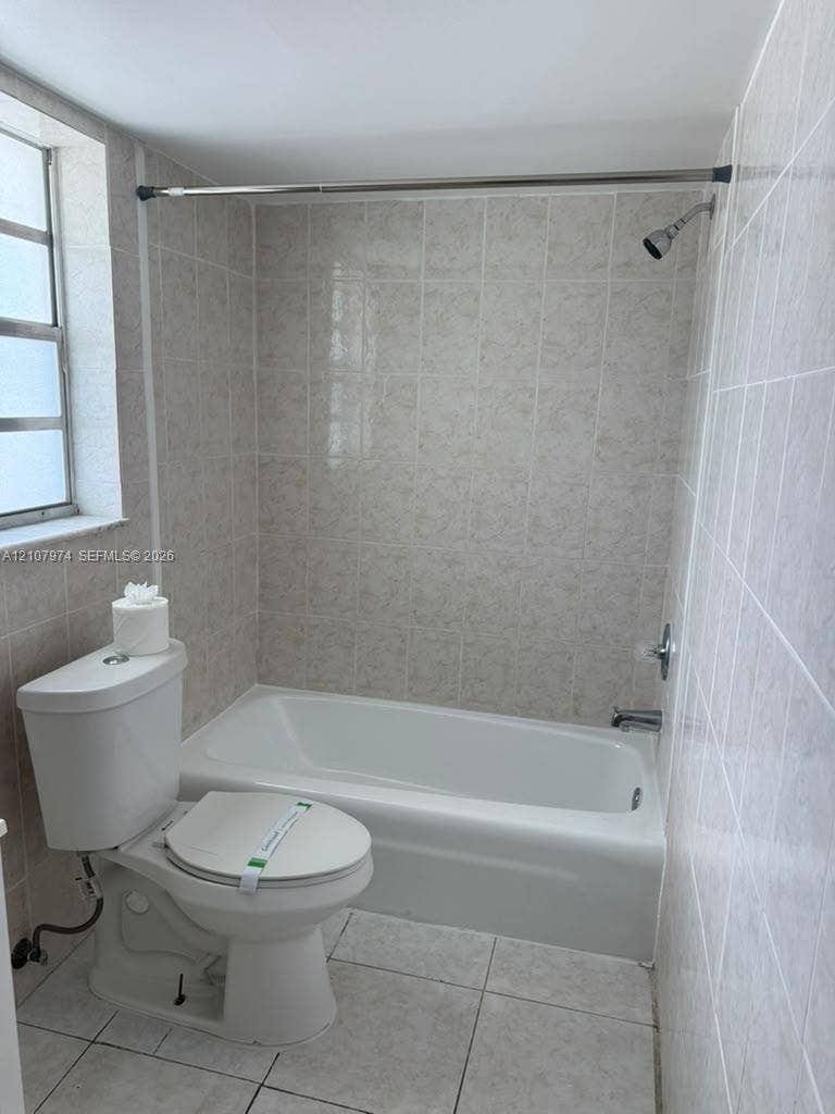 Full-height neutral wall tiling, bathtub and shower combination, ceramic floor tile, and multi-pane window