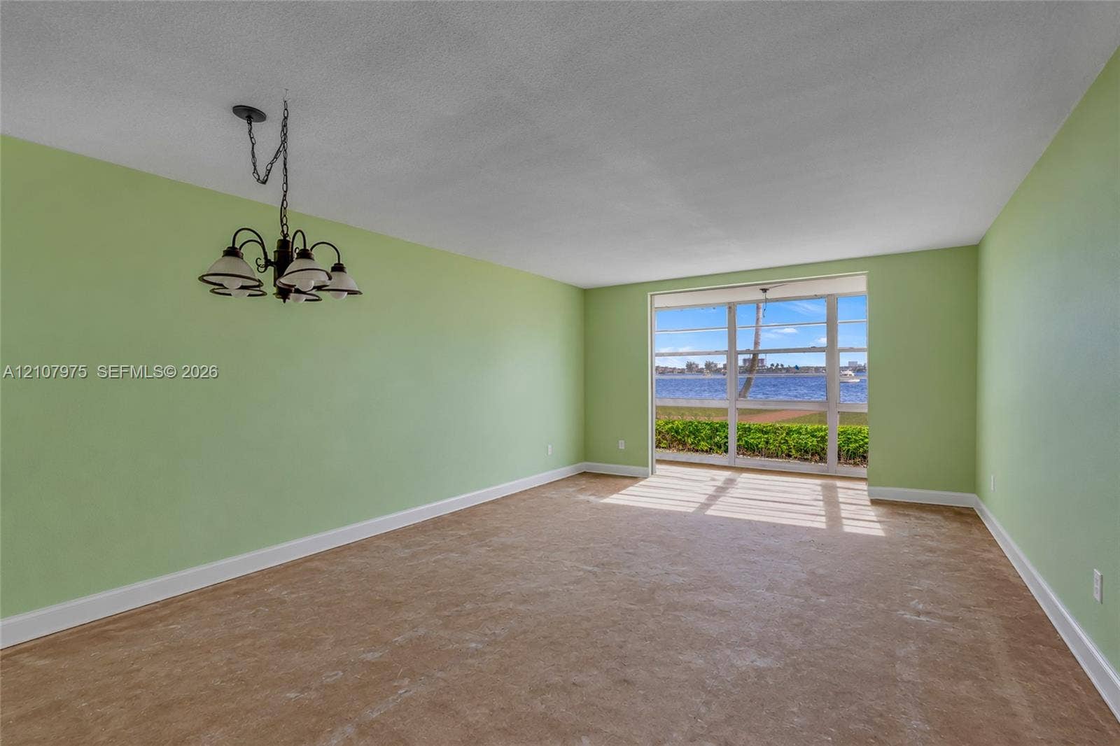 2910 Point East Drive, #M108, Aventura, FL 33160 Spacious room featuring floor-to-ceiling windows with water exposure, wall-to-wall carpeting, and a multi-arm metal chandelier
