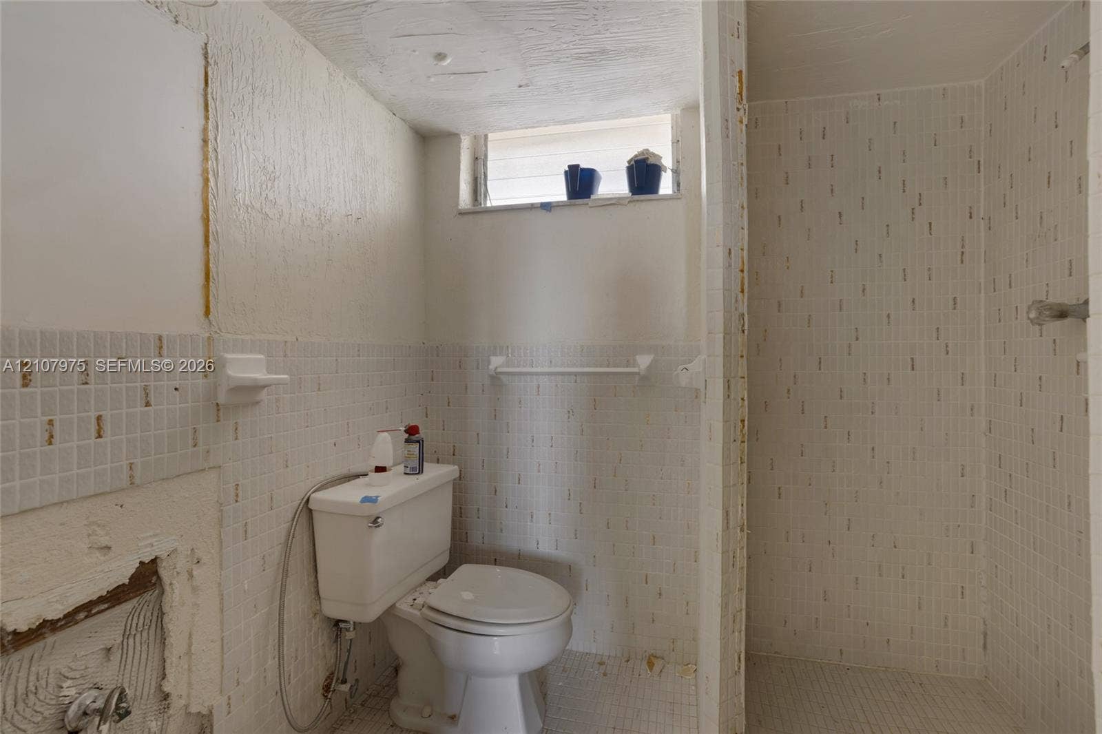 2910 Point East Drive, #M108, Aventura, FL 33160 Bathroom featuring square white wall tiling, a built-in shower enclosure, a white porcelain toilet, and a recessed window