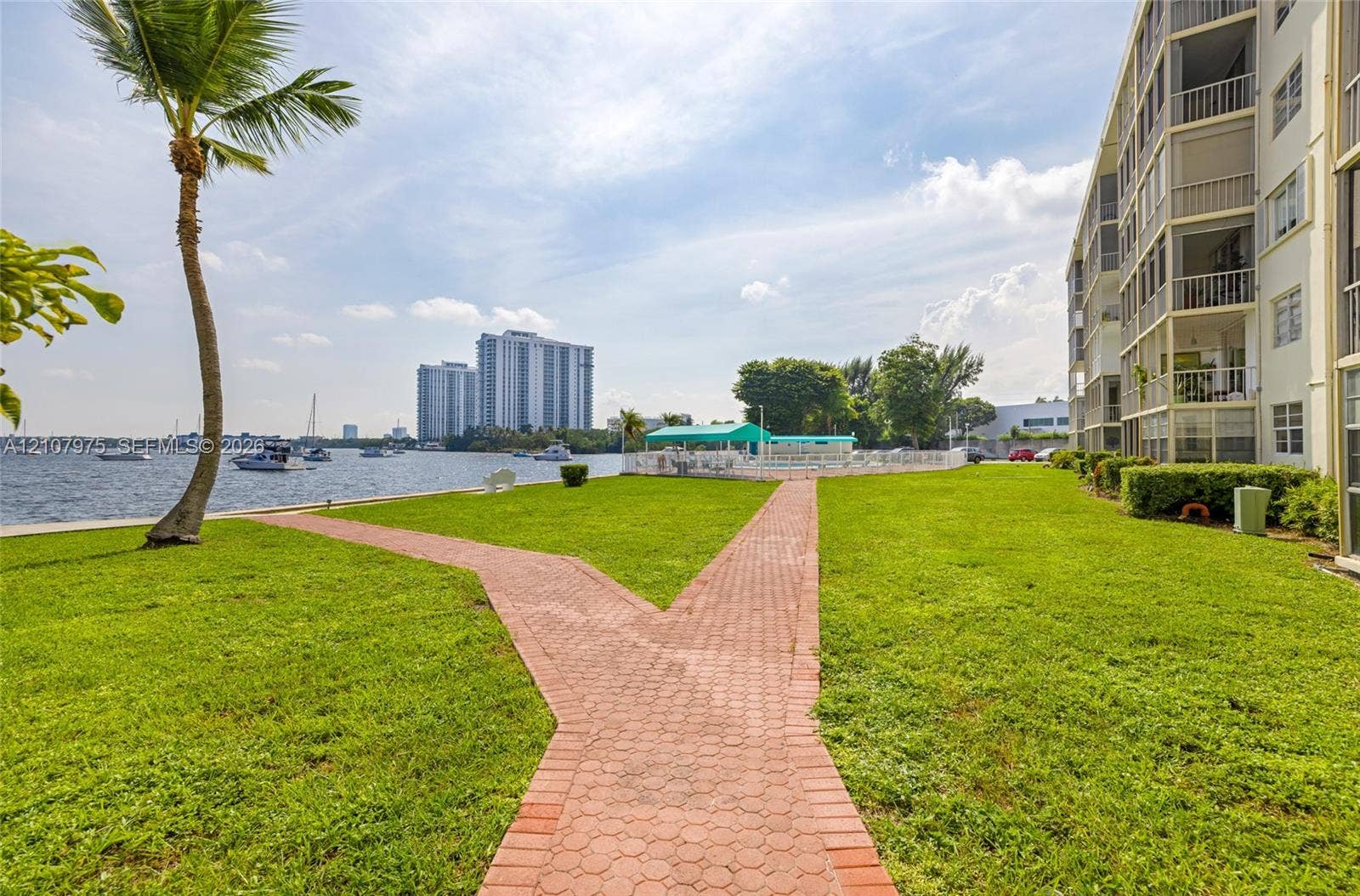 2910 Point East Drive, #M108, Aventura, FL 33160 Waterfront grounds featuring manicured lawn, brick paver pathway, and exterior balcony structures