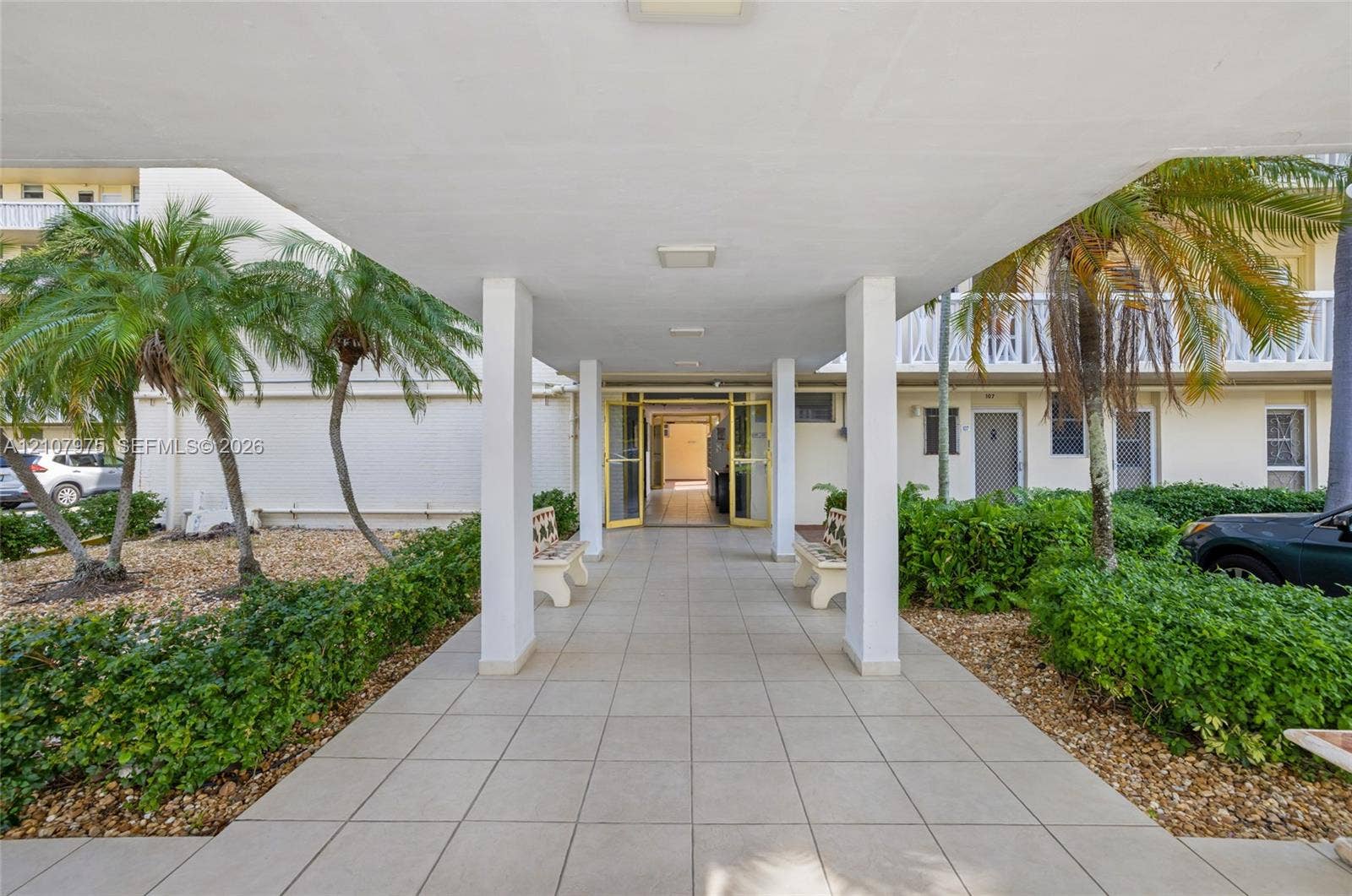 2910 Point East Drive, #M108, Aventura, FL 33160 Covered entrance featuring large-format ceramic floor tiles, square support pillars, integrated ceiling lighting, and flanking landscaping