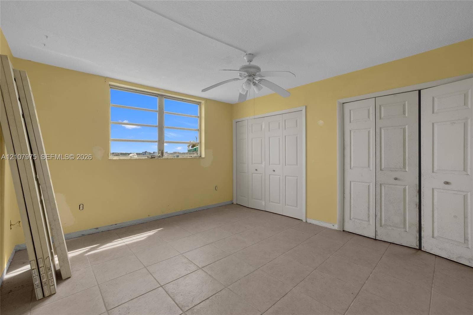 2910 Point East Drive, #M108, Aventura, FL 33160 Interior space featuring tile flooring, dual bi-fold door closets, a multi-pane window, and a ceiling fan with integrated lighting