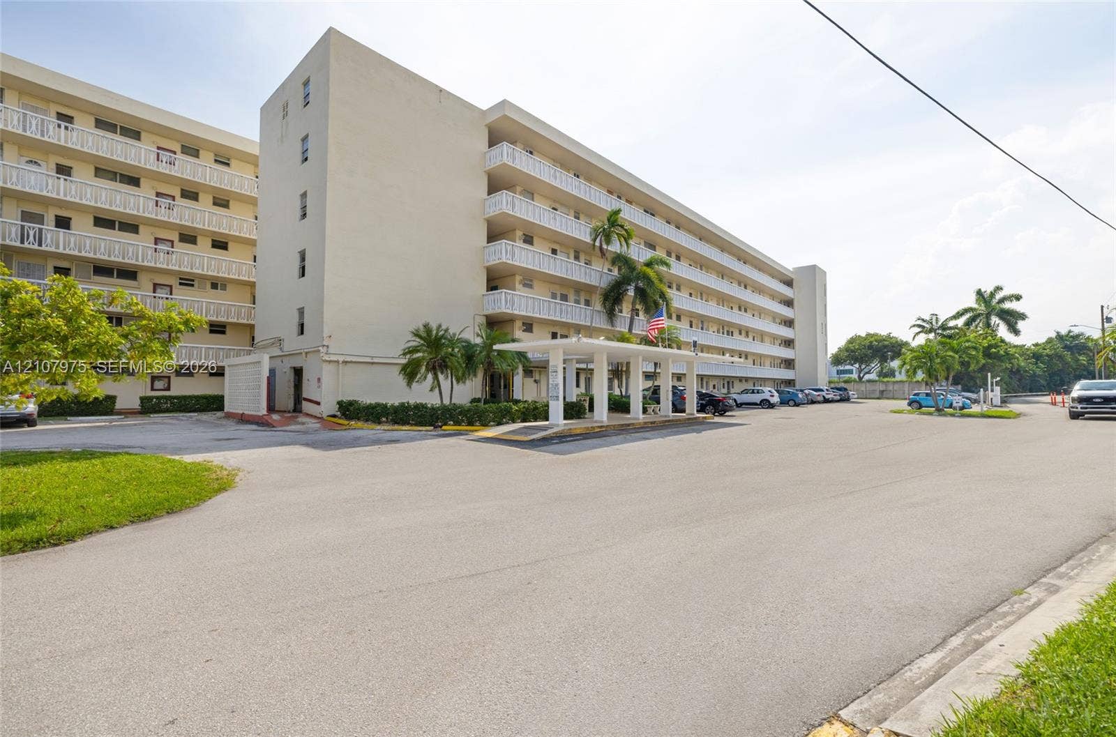 2910 Point East Drive, #M108, Aventura, FL 33160 Multi-story exterior featuring a covered porte-cochre, balcony railings on each level, and integrated landscaping with mature palm trees
