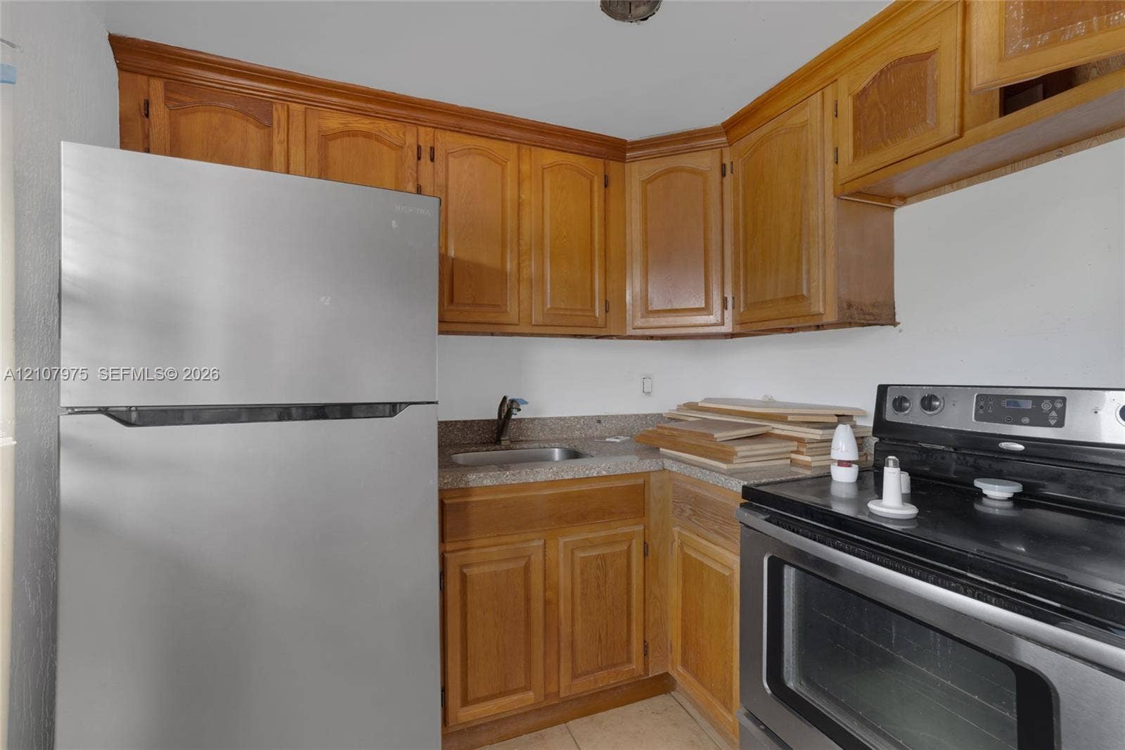 2910 Point East Drive, #M108, Aventura, FL 33160 Kitchen featuring natural wood-finish cabinetry, speckled stone-composite countertops, stainless steel refrigerator, and a stainless steel electric range