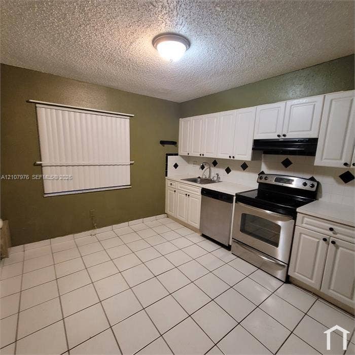 5100 SW 41st Street, #101, Hollywood, Hollywood, FL 33023 Kitchen featuring white cabinetry, stainless steel appliances, ceramic tile flooring, and a tiled backsplash with decorative accents