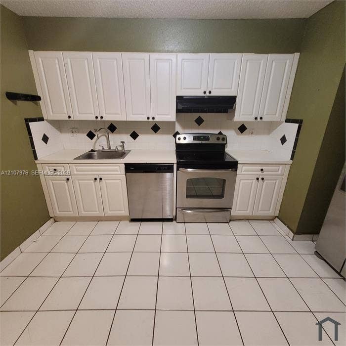 5100 SW 41st Street, #101, Hollywood, Hollywood, FL 33023 Kitchen featuring white shaker-style cabinetry, stainless steel dishwasher and range, solid-surface countertops, and ceramic tile flooring