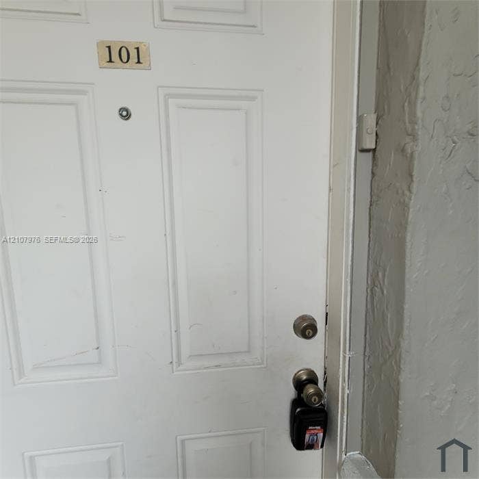 5100 SW 41st Street, #101, Hollywood, Hollywood, FL 33023 White six-panel entry door with brass-tone hardware, integrated peephole, and door-mounted identification plaque