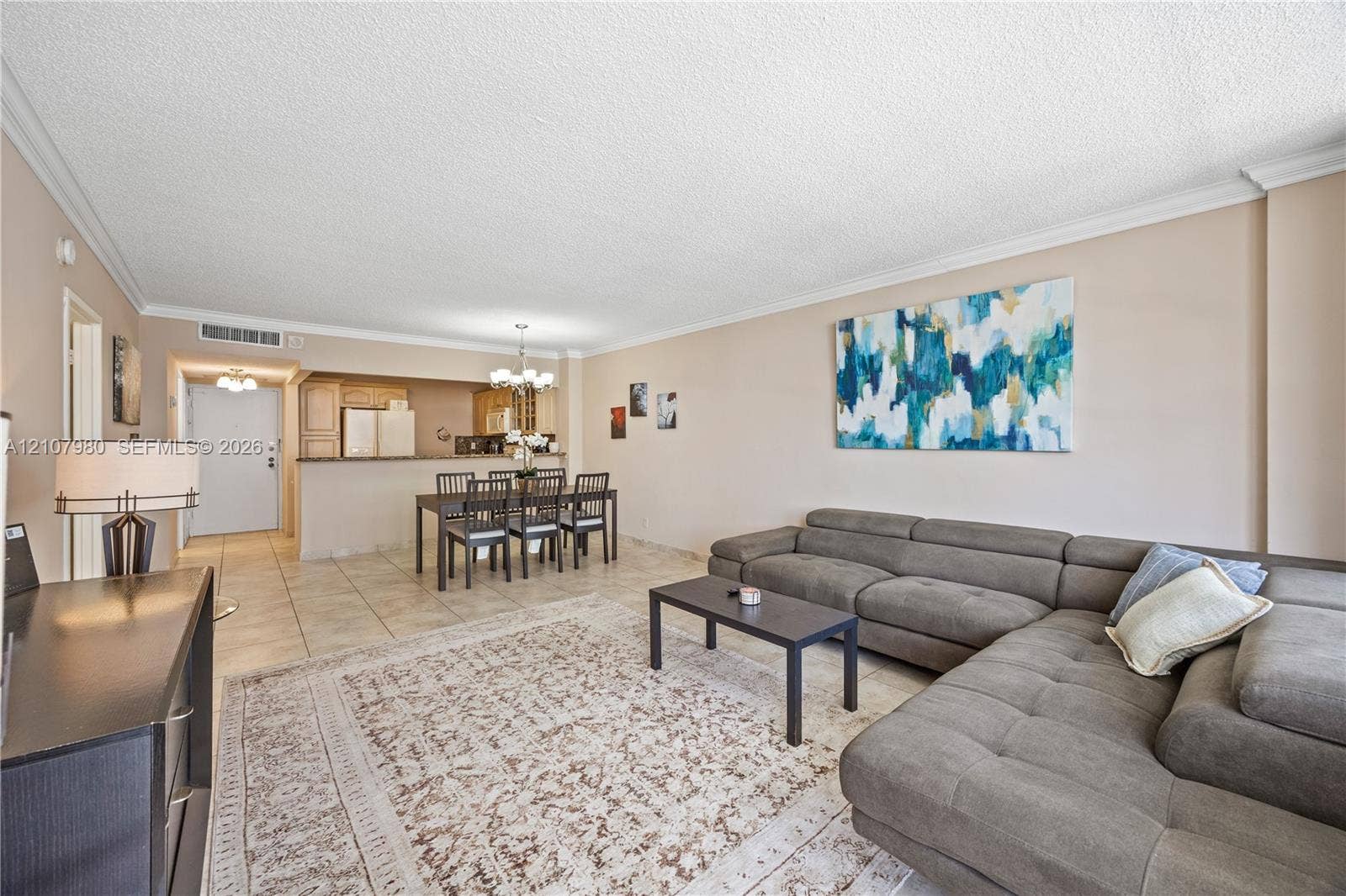 3725 S Ocean Drive, #1120, Hollywood, Hollywood, FL 33019 Open-concept interior featuring large-format neutral floor tiles, crown molding, a kitchen pass-through, and a decorative chandelier