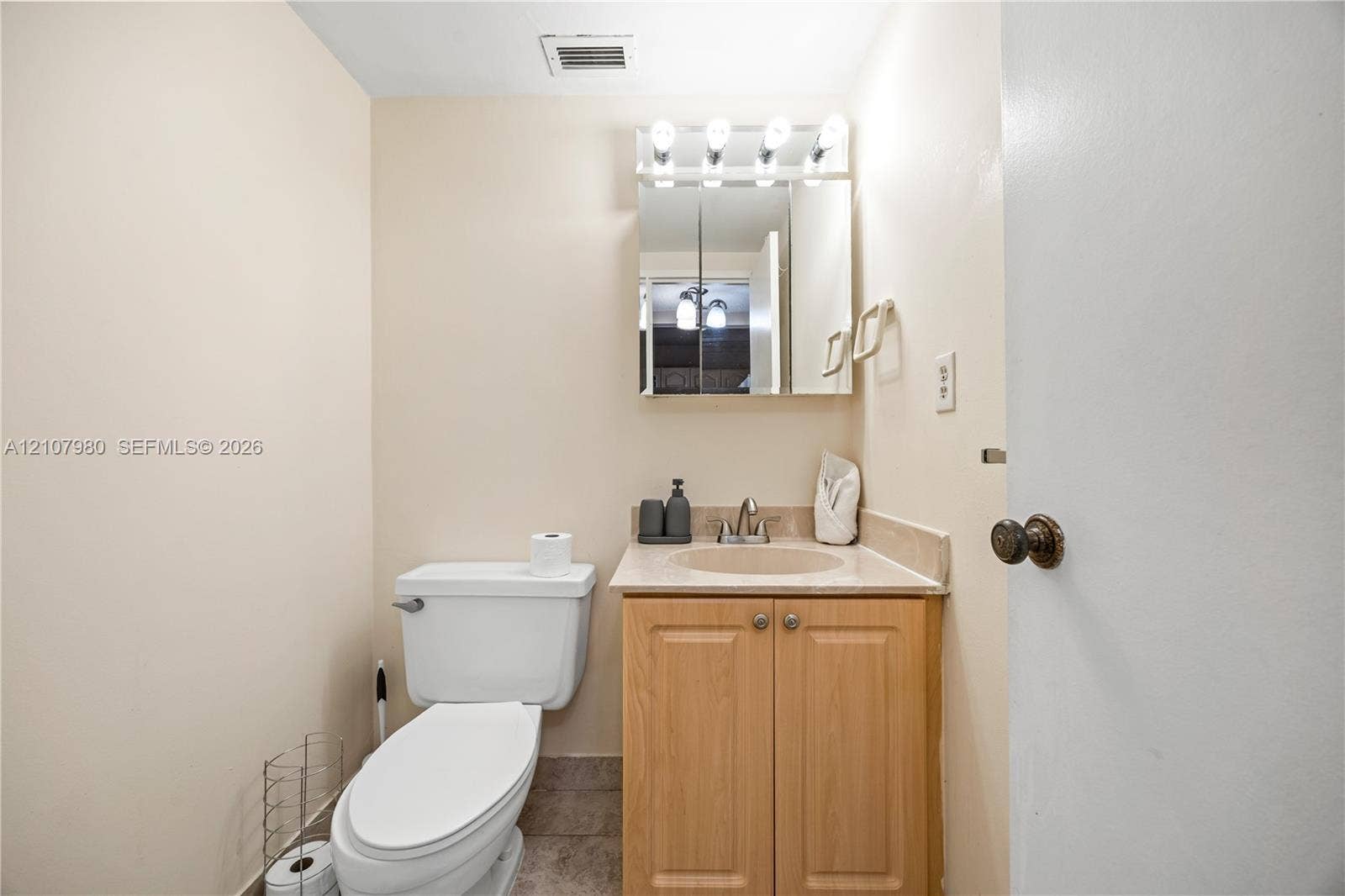 3725 S Ocean Drive, #1120, Hollywood, Hollywood, FL 33019 Light-toned wood vanity with a solid-surface integrated sink, mirrored medicine cabinet with integrated lighting, and a neutral-toned toilet
