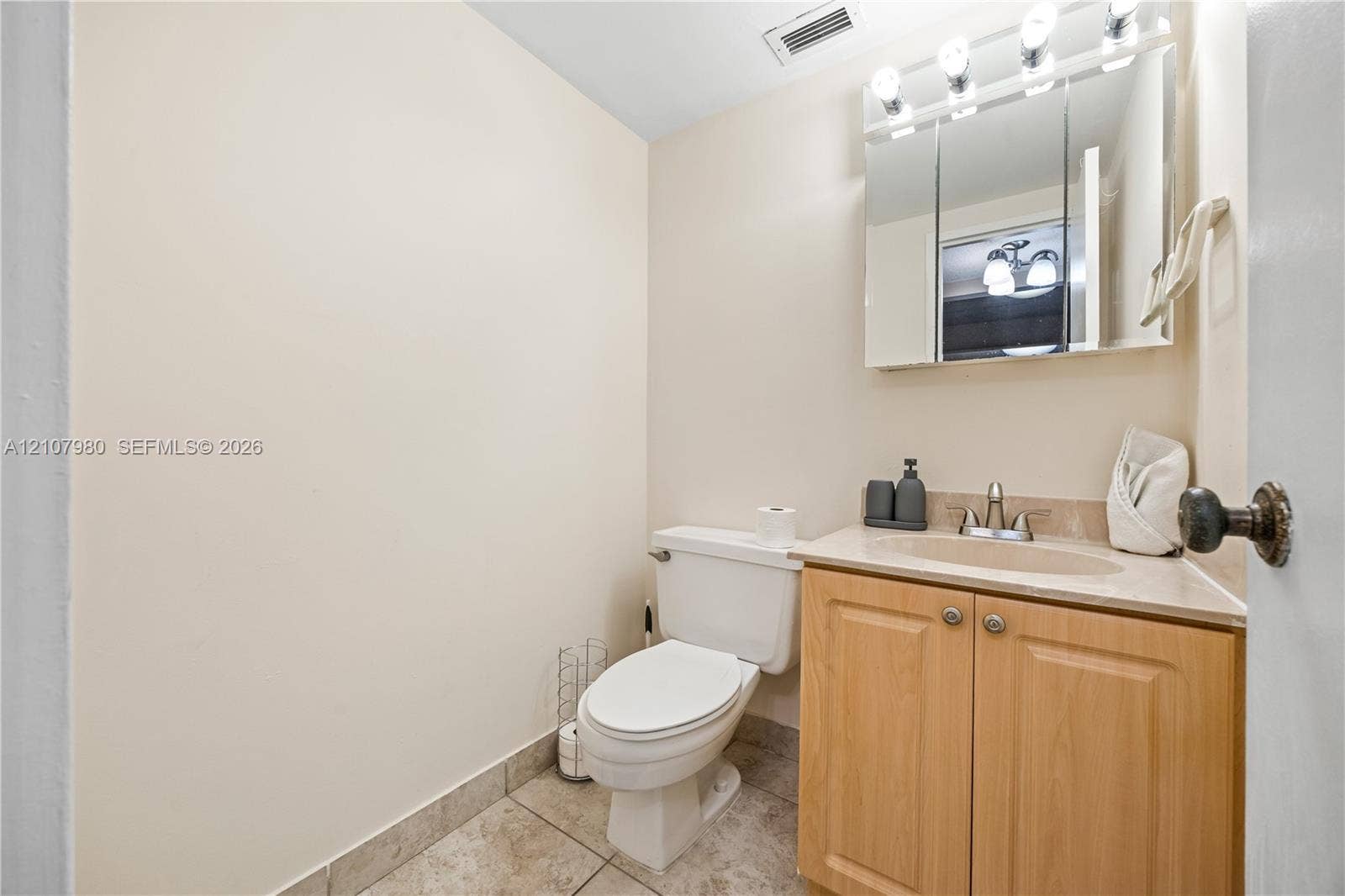 3725 S Ocean Drive, #1120, Hollywood, Hollywood, FL 33019 Vanity featuring light wood-finish cabinetry, a neutral-toned countertop with an integrated oval sink, a tri-panel mirrored medicine cabinet, and tile flooring