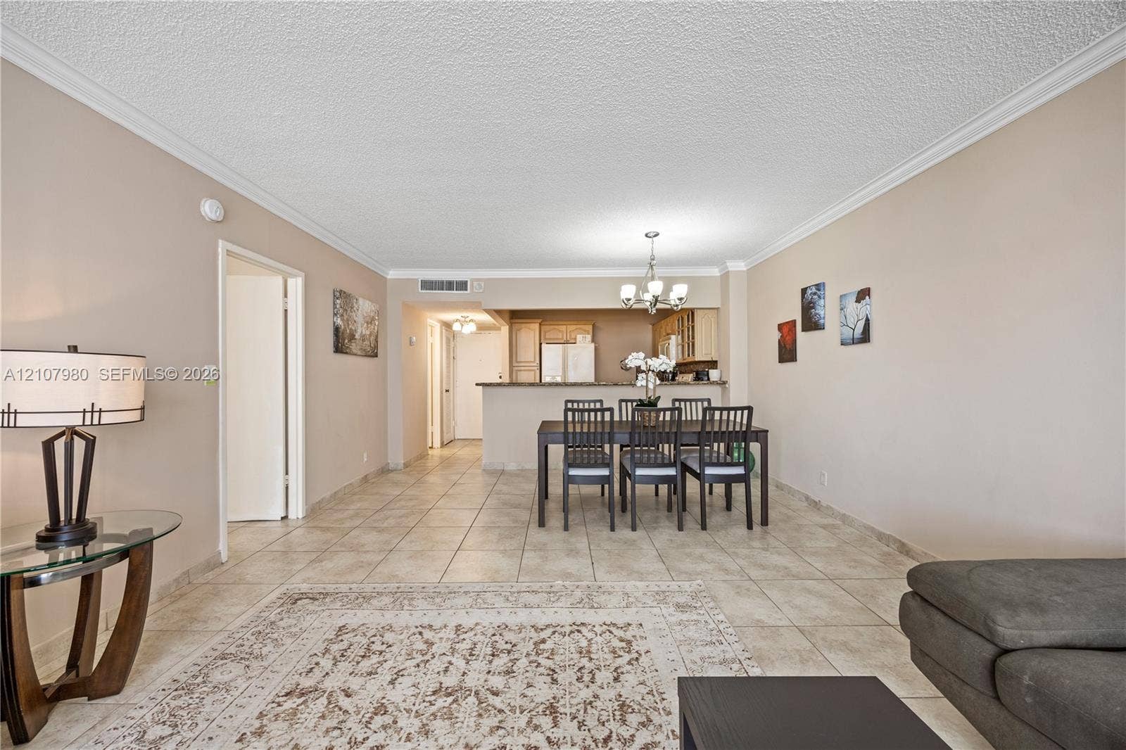 3725 S Ocean Drive, #1120, Hollywood, Hollywood, FL 33019 Open-concept living space featuring ceramic tile flooring, crown molding, a kitchen pass-through counter, and a multi-arm chandelier