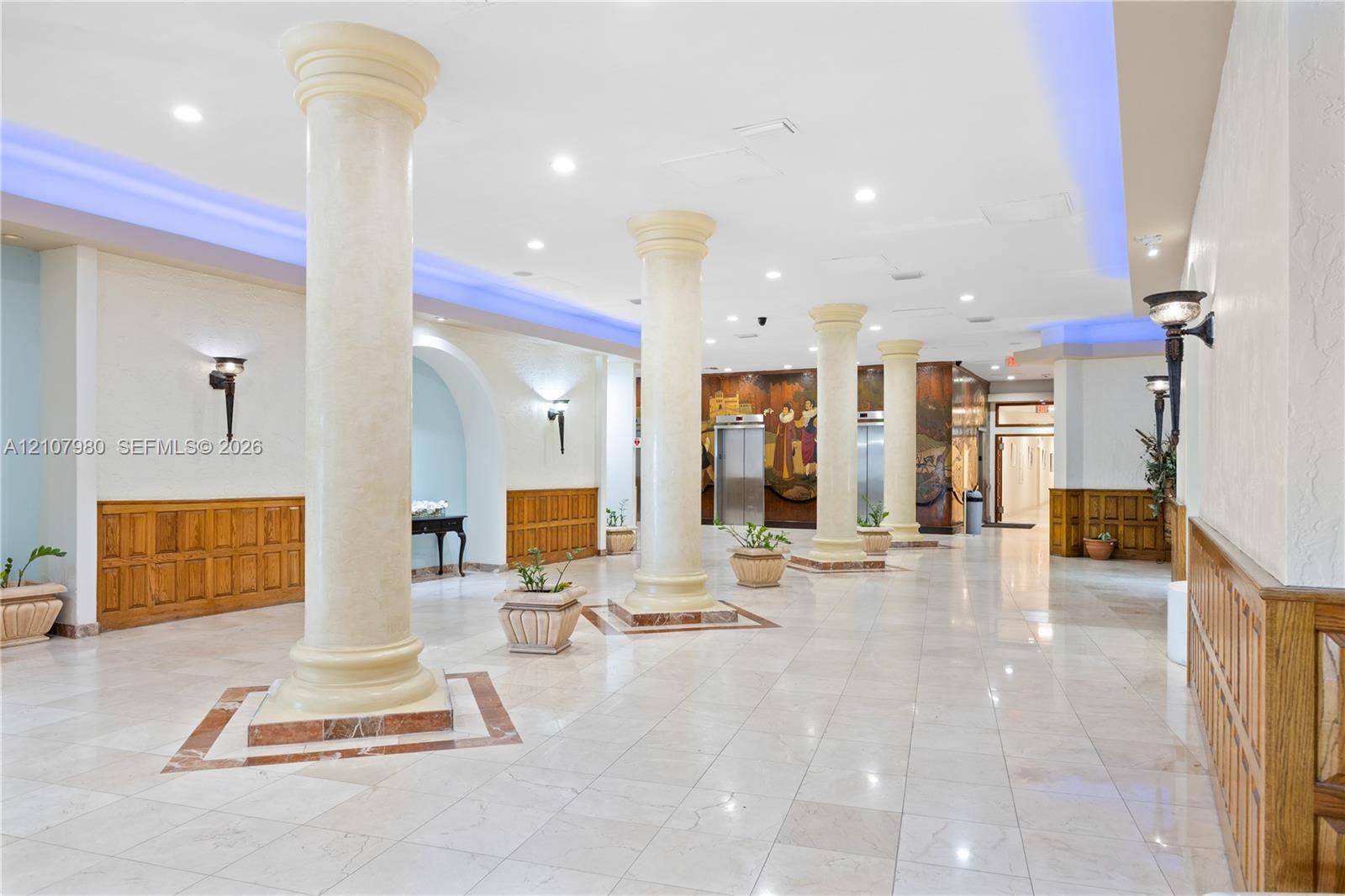 3725 S Ocean Drive, #1120, Hollywood, Hollywood, FL 33019 Grand lobby featuring polished stone flooring, architectural columns, wall-mounted sconces, wood-panel wainscoting, and metallic-finish elevator doors